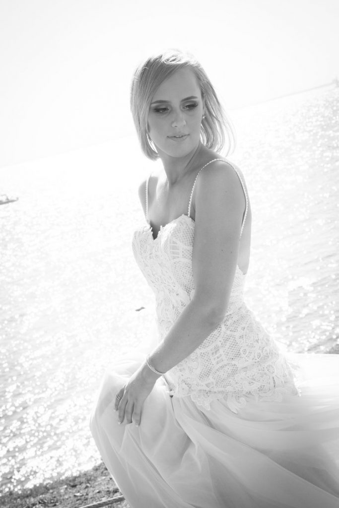 Black and white outdoor portrait of a bride in a lace wedding dress gently holding her veil.