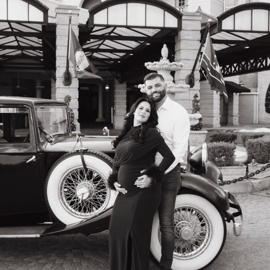 Pregnant woman in a burgundy dress posing beside a vintage dark blue car at The Jefferson Hotel in Richmond, Virginia.