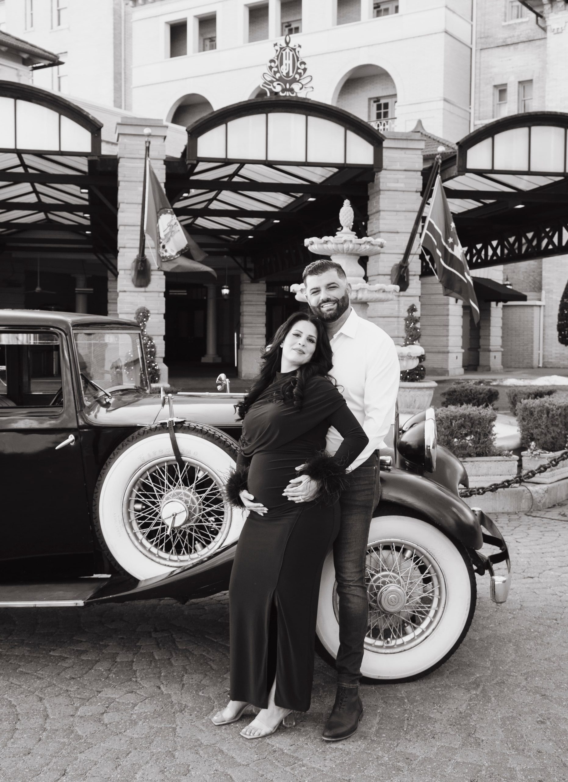 Pregnant woman in a burgundy dress posing beside a vintage dark blue car at The Jefferson Hotel in Richmond, Virginia.